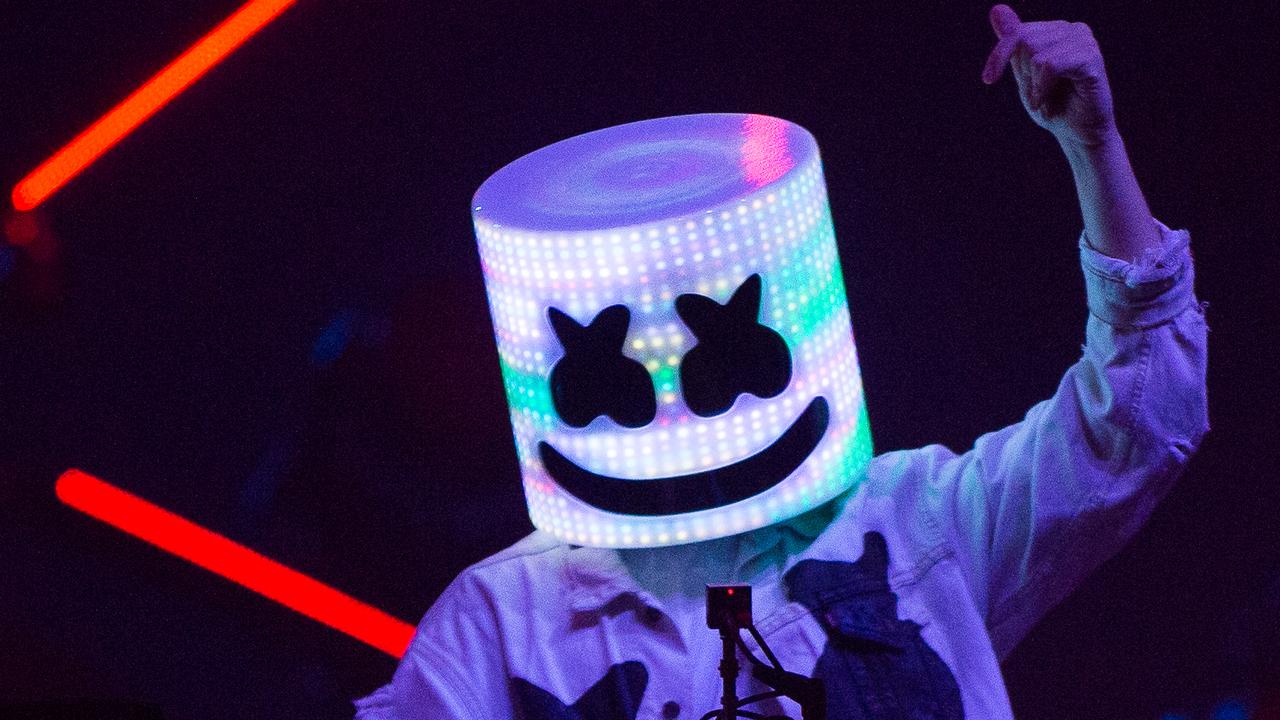 Superstar DJ Marshmello wearing his iconic mask with LEDs lighting up the mask,. The background is black with red strobes. The DJ hid his NFT portfolio.