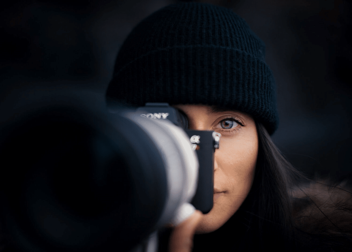The picture depicts a female photographer named Cath Simard with a camera in front of her