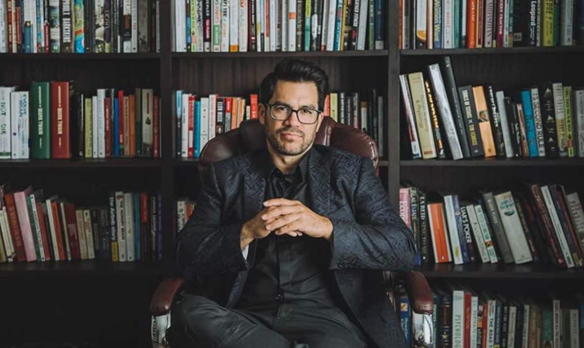 The picture depicts Tai Lopez in a library
