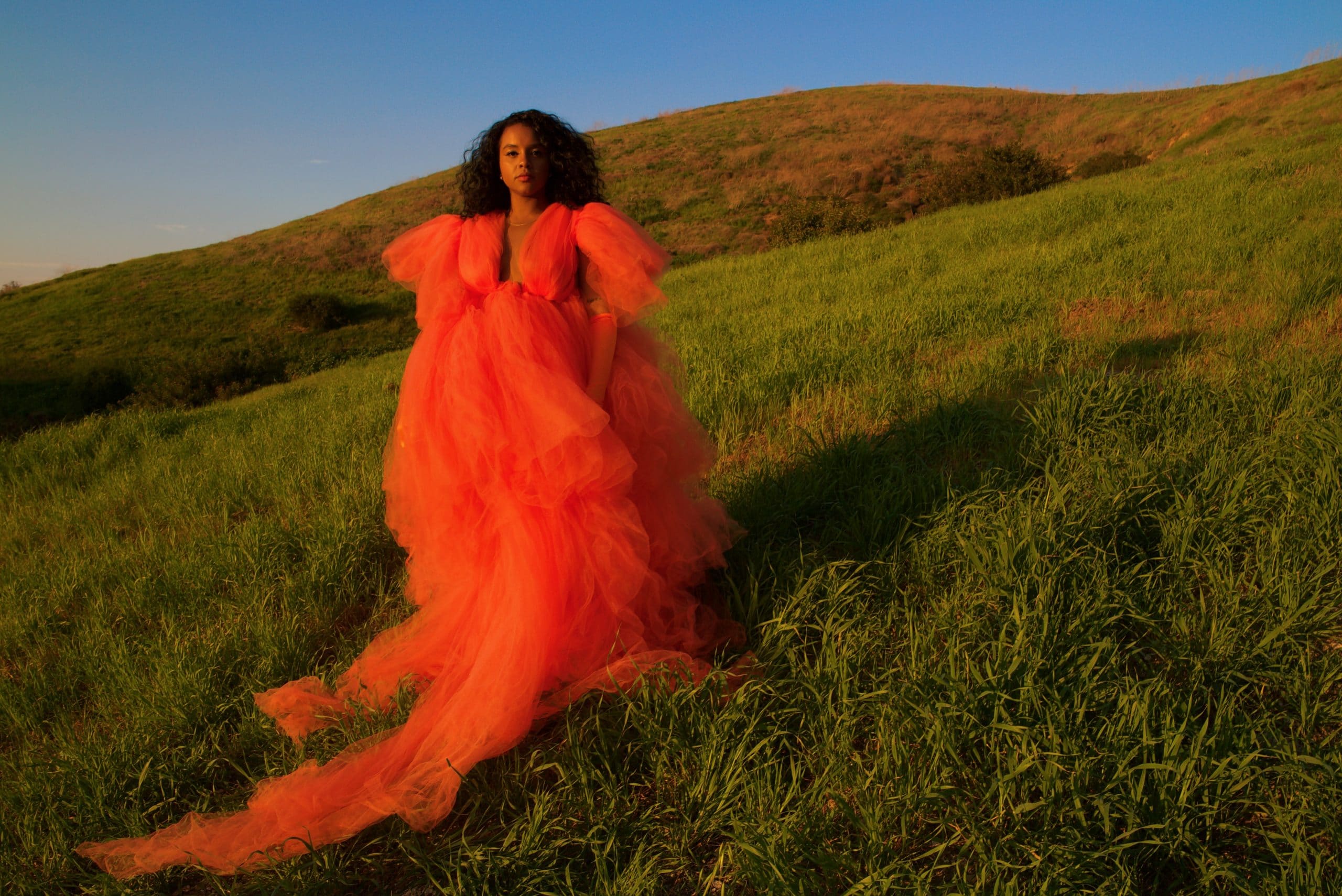 Latasha standing in a field wearing an orange dress