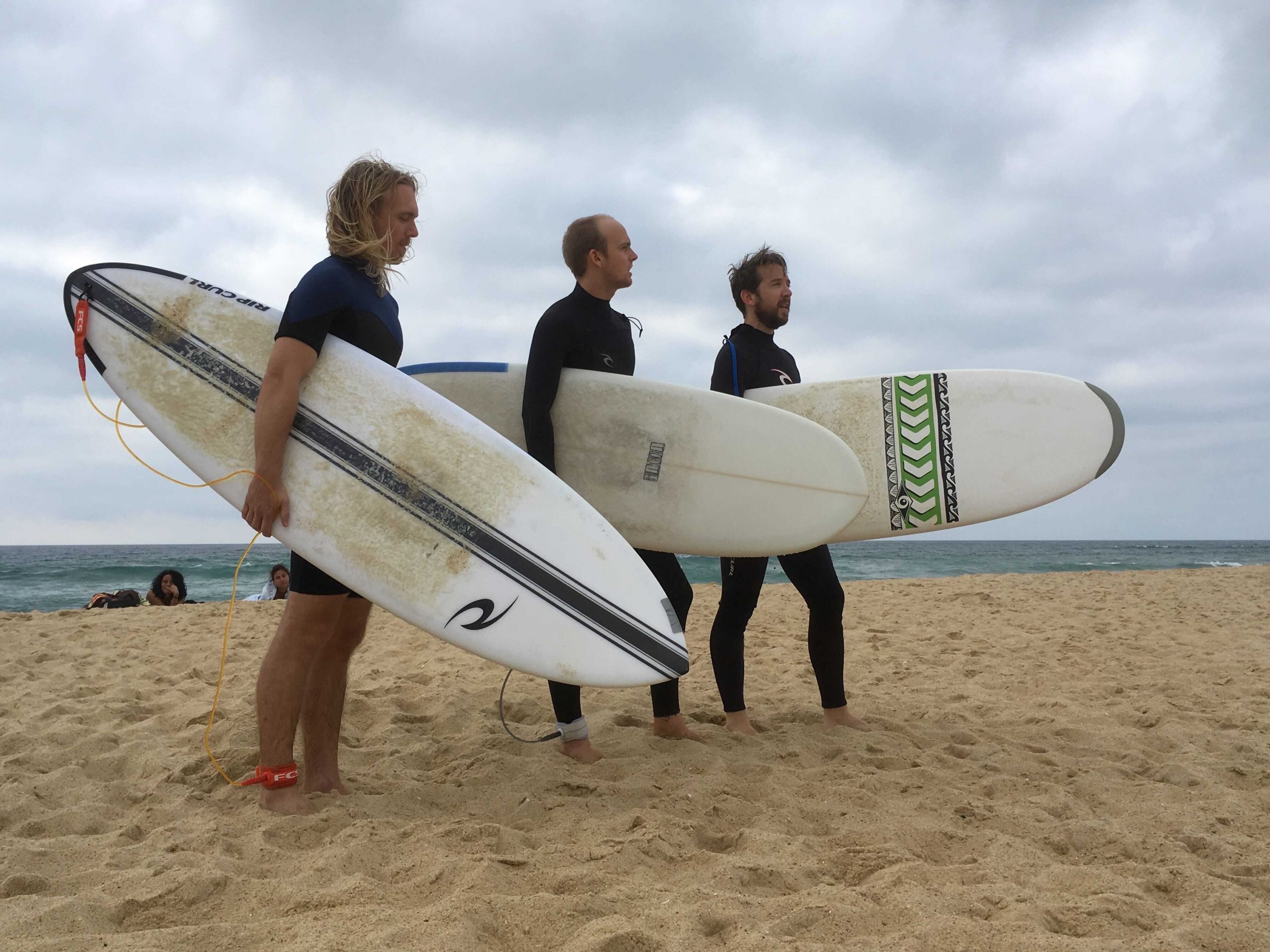 SuperRare founders standing on a beach holding surfboards