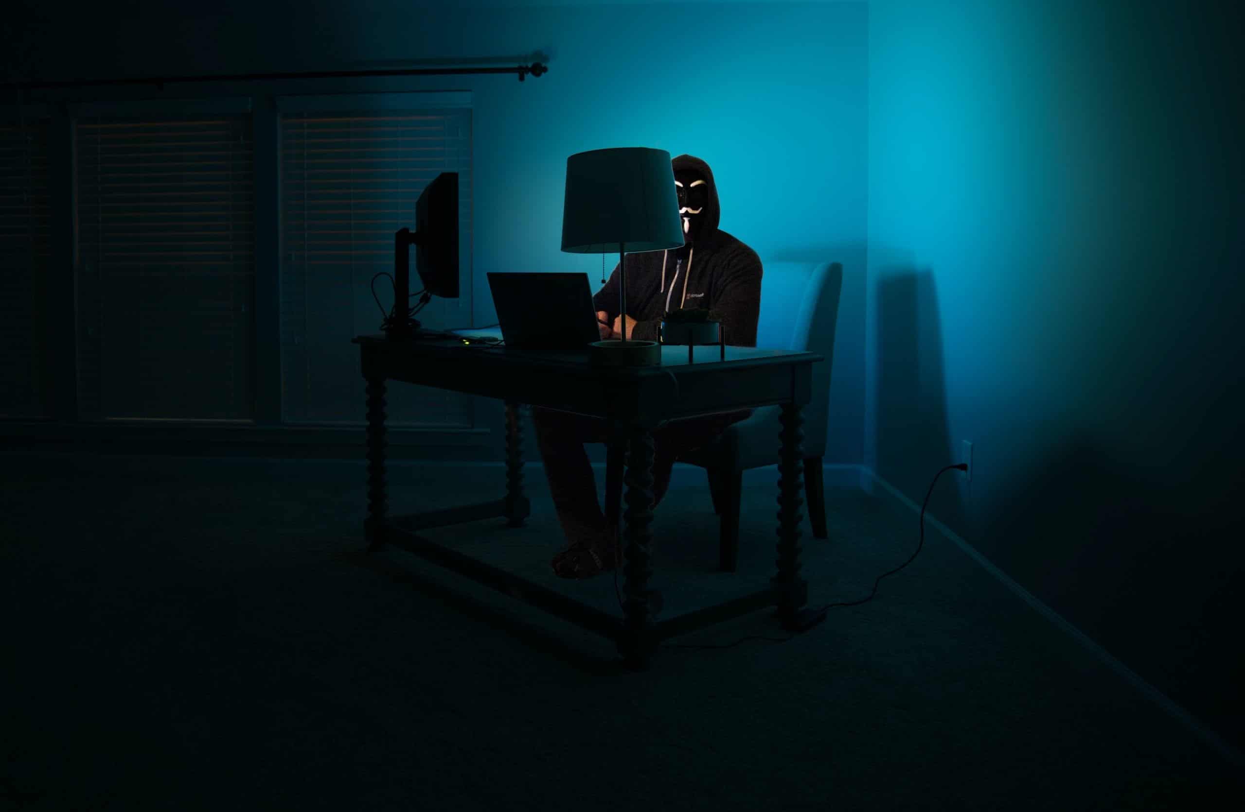 The picture shows a hacker in a dim lit room