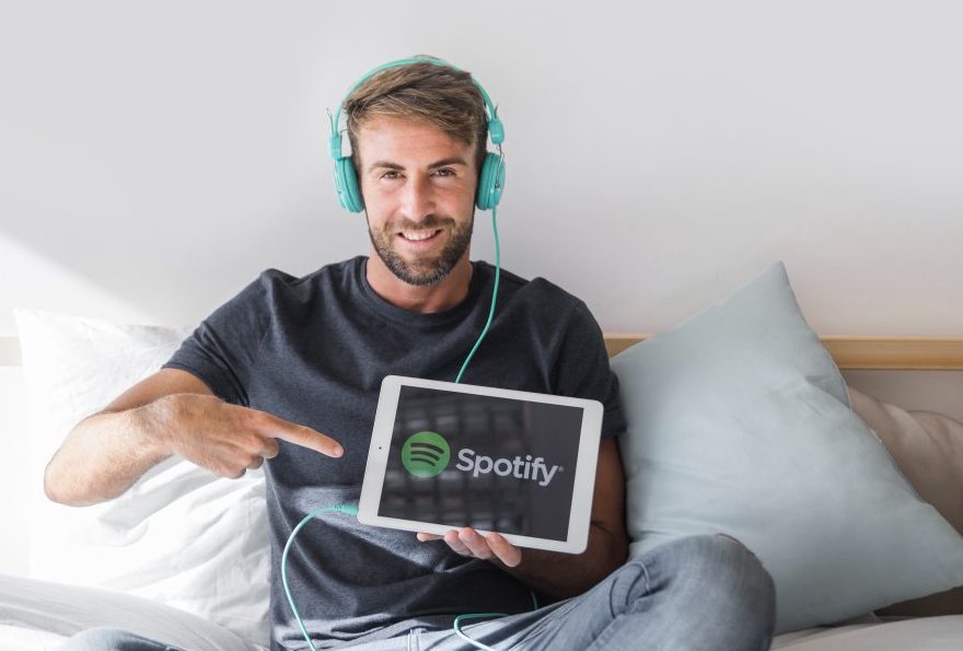 image of a man wearing headphones while holding a tablet with Spotify logo