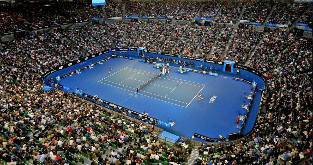 Una cancha de tenis azul está rodeada por un estadio lleno de gente.  Esto es en el Asutralian Open, donde los NFT de 2022 vienen con el beneficio de entradas gratuitas para la semana de finales.