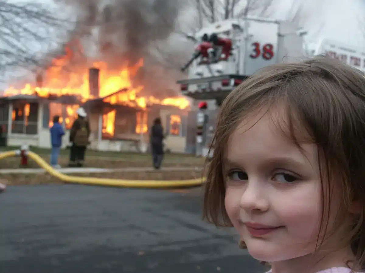 disaster girl meme with house burning in the background