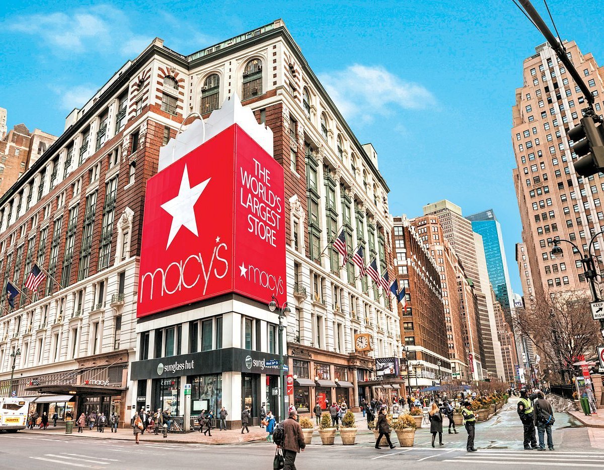 The Macy's store in downtown New York City is pictured with people walking in front. It appears to be autumn, in support of Macy's Thanksigiving Day Parade metaverse event.