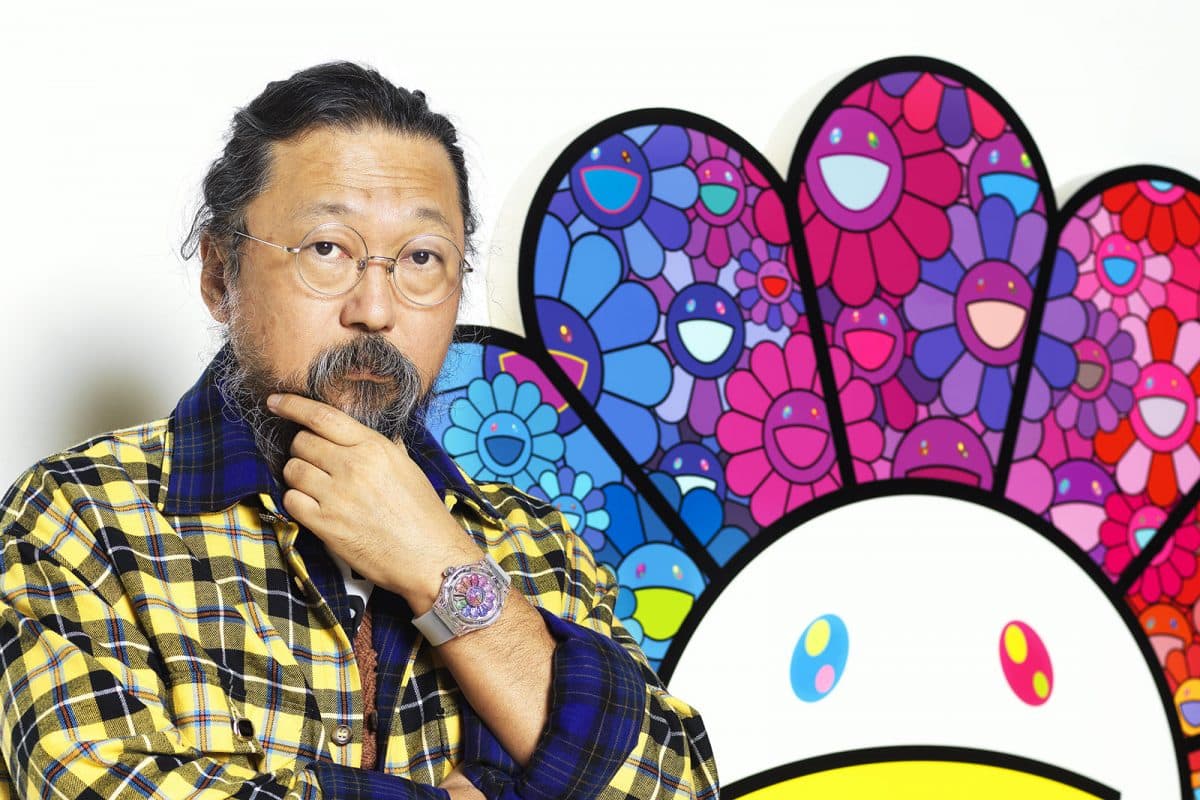 Takashi Murakami stands in front of a multi-color smiling face with a Hublot watch in support of the Murakami X Hublot release.