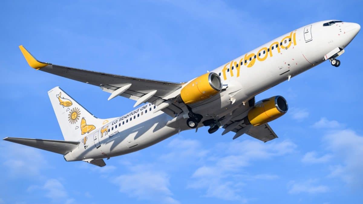 A white plane with yellow Flybondi texts soars through the sky.